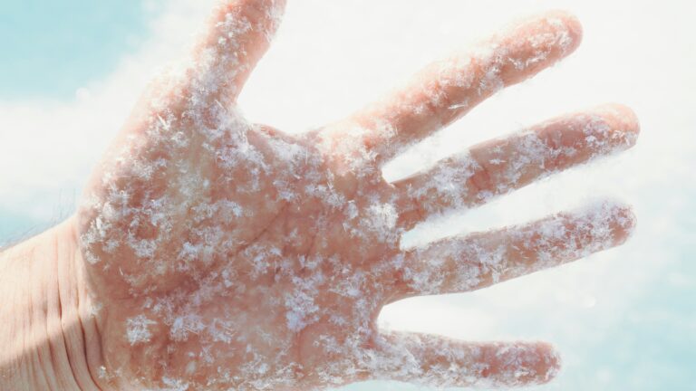 a person's hand covered in snow against a blue sky