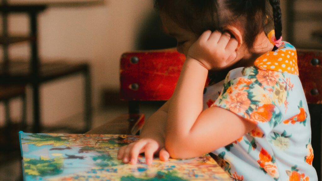 a little girl sitting at a table with a book