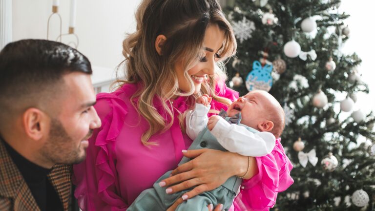 Parents holding their newborn baby near christmas tree