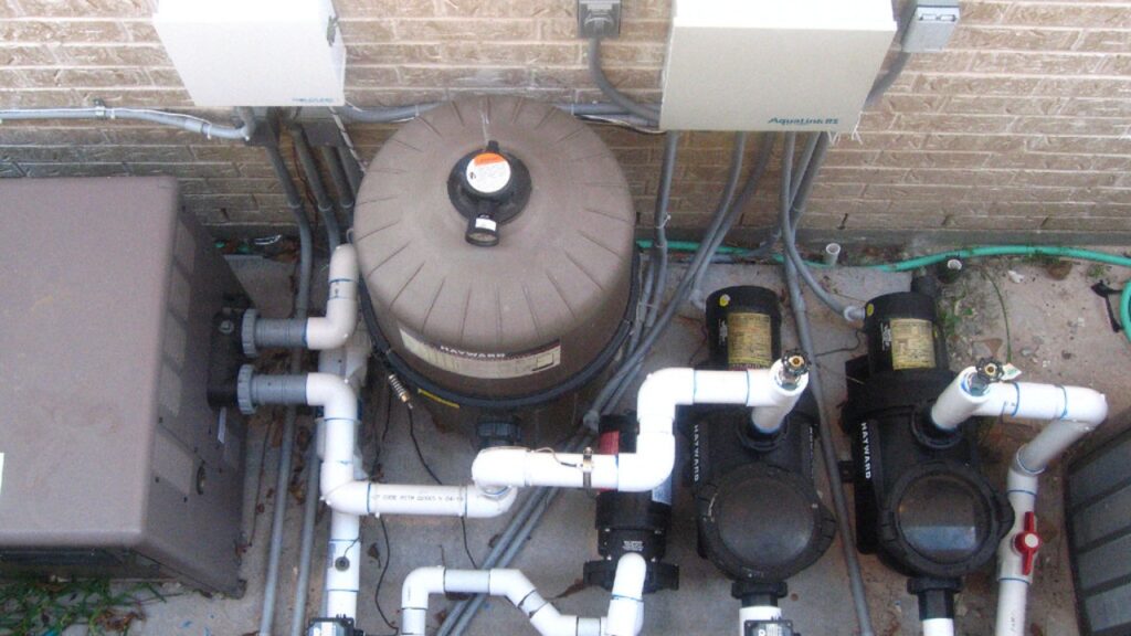 A backyard pool equipment pad with Hayward-branded pumps and a filter housing