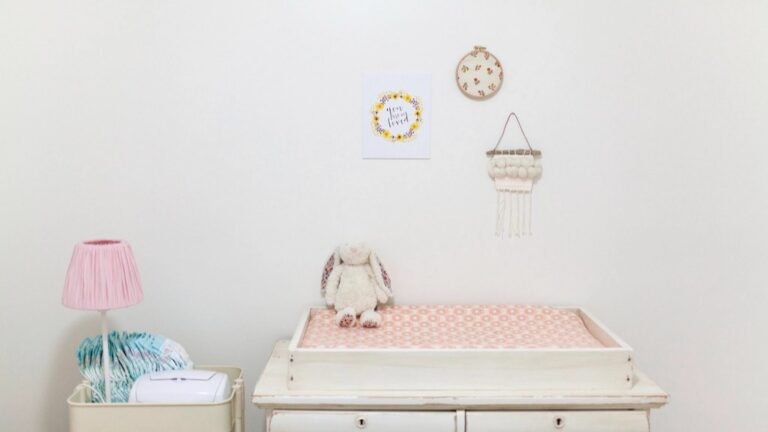 A softly lit nursery changing station with a pink pad, a stuffed rabbit, and diaper storage, generic and unbranded
