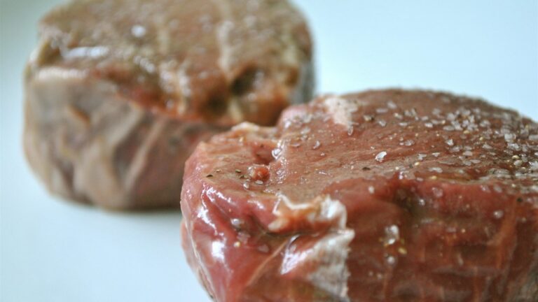 Two raw seasoned beef steaks on a white plate