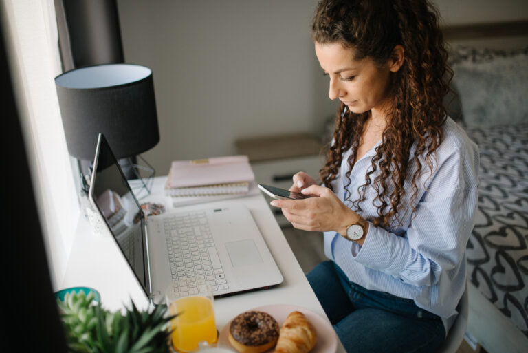 A woman looks at her smartphone while working at home