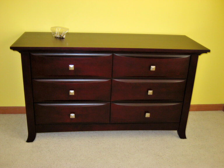A dark wood six-drawer dresser against a yellow wall