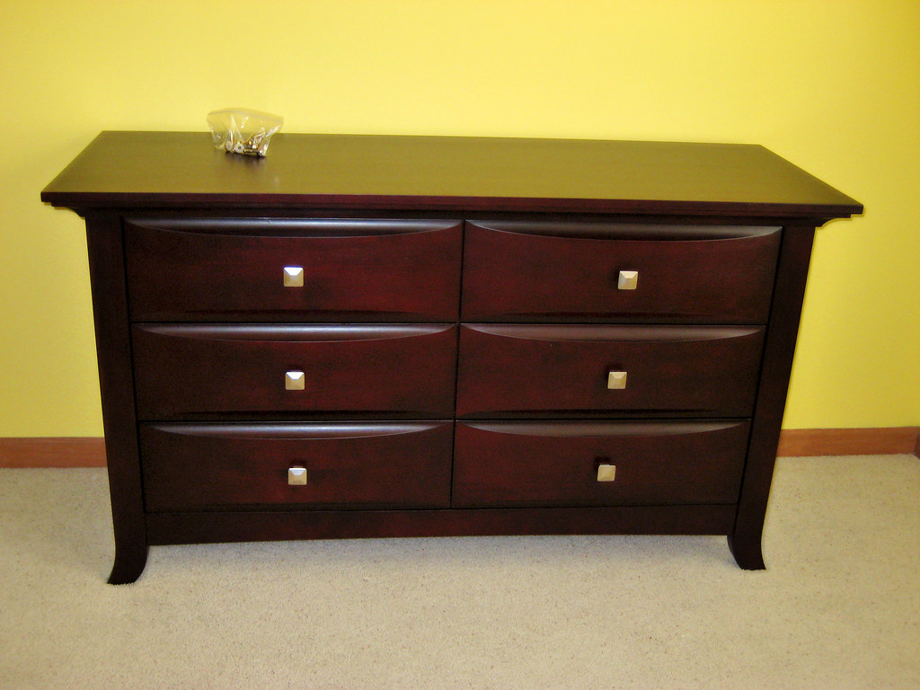 A dark wood six-drawer dresser against a yellow wall