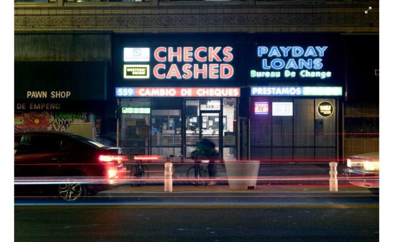 Neon "Checks Cashed" and "Payday Loans" signs on a storefront at night