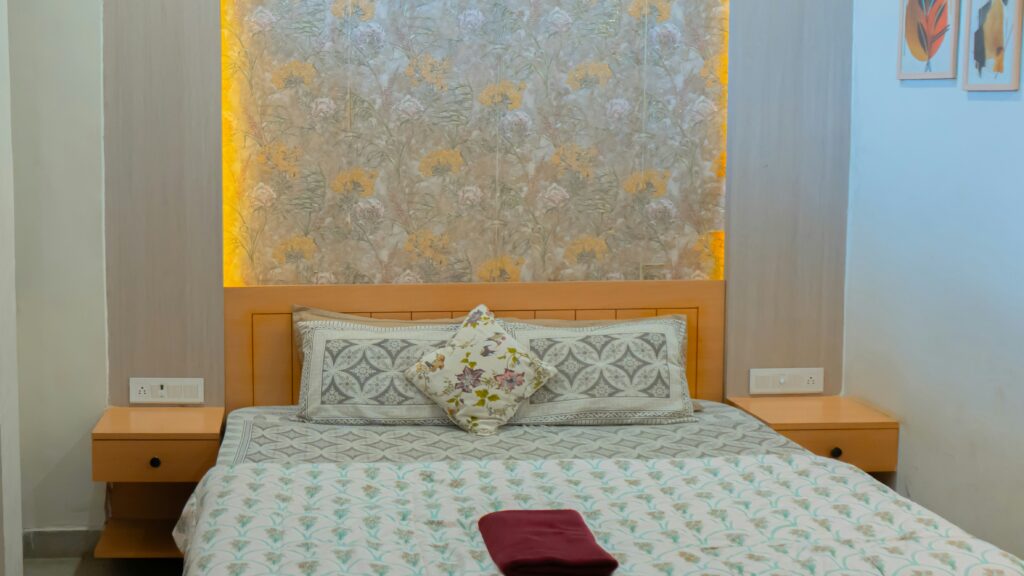 A bed with patterned bedding and pillows against a floral wallpaper headboard