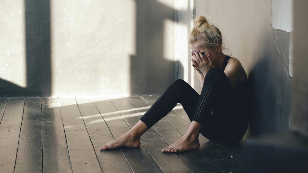 Woman sitting on floor, covering face with hands