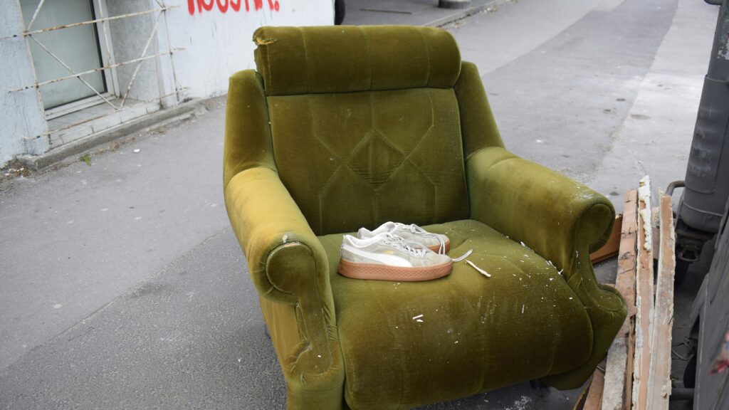 An old green armchair sits on a sidewalk