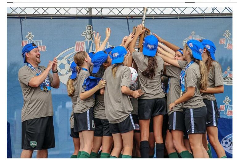 A girls' youth soccer team celebrates with their coach after winning a national championship