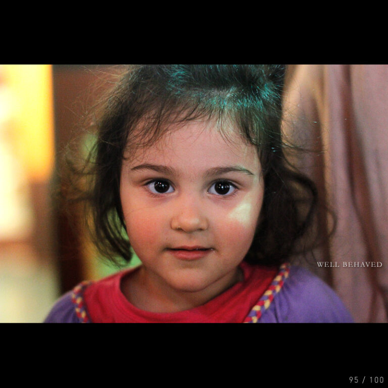 A young girl sitting quietly with a shy, thoughtful expression