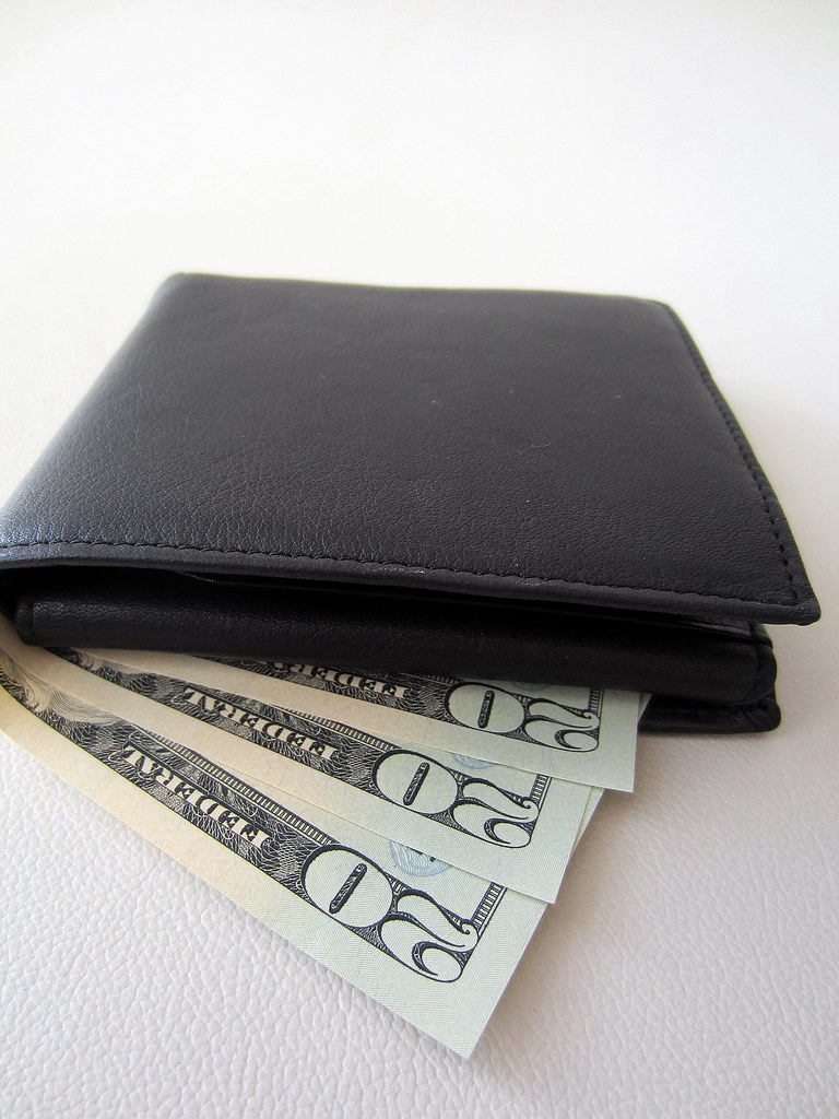 A black leather wallet with visible U.S. twenty dollar bills